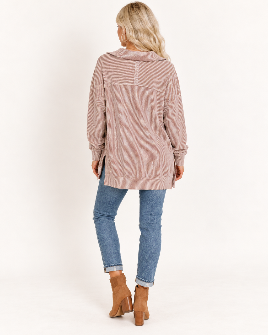 A woman shown from the back wearing a dusty rose long-sleeve hooded sweatshirt, blue skinny jeans, and brown ankle boots, photographed against a clean white studio background.
