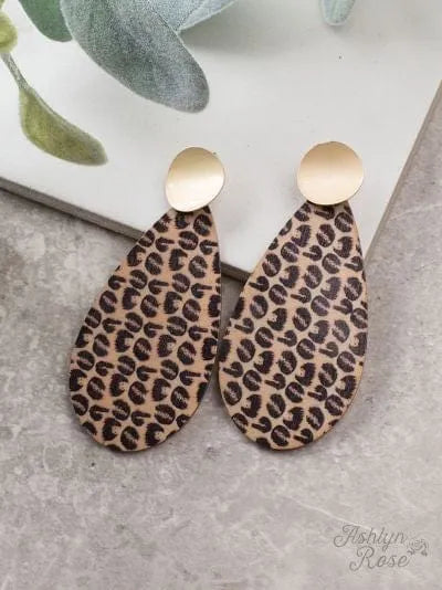 Knock on Wood wooden leopard print and gold drop earrings on gray surface with green leaves background