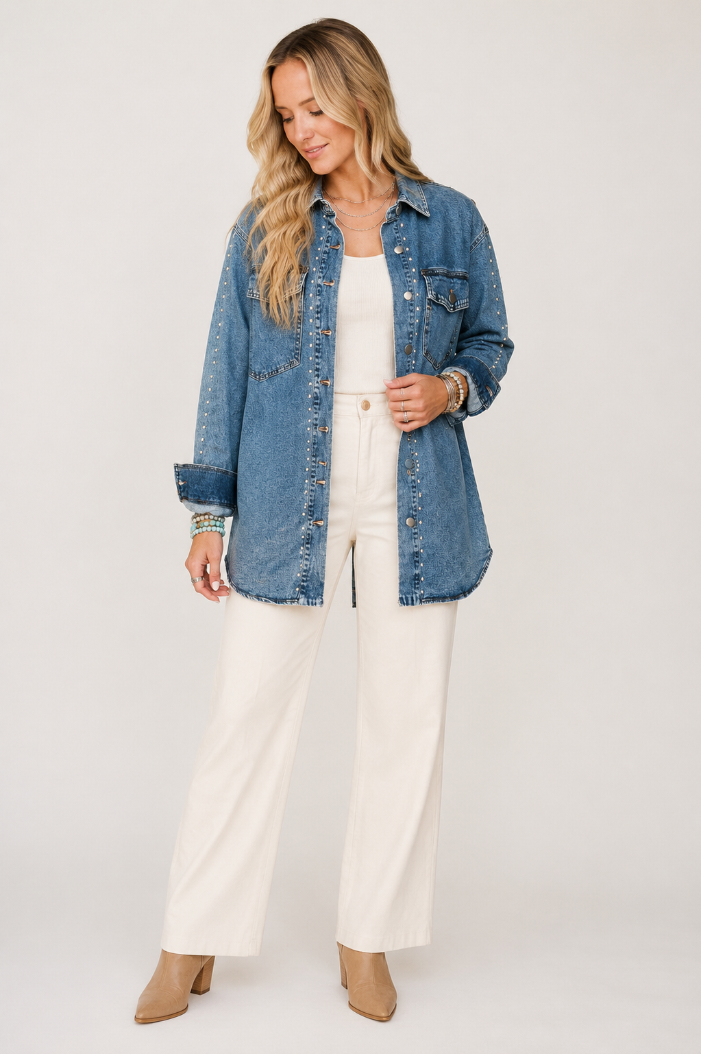 Blonde model wearing the Silver Spur sail-blue studded longline denim jacket with ivory trousers on a warm white background.