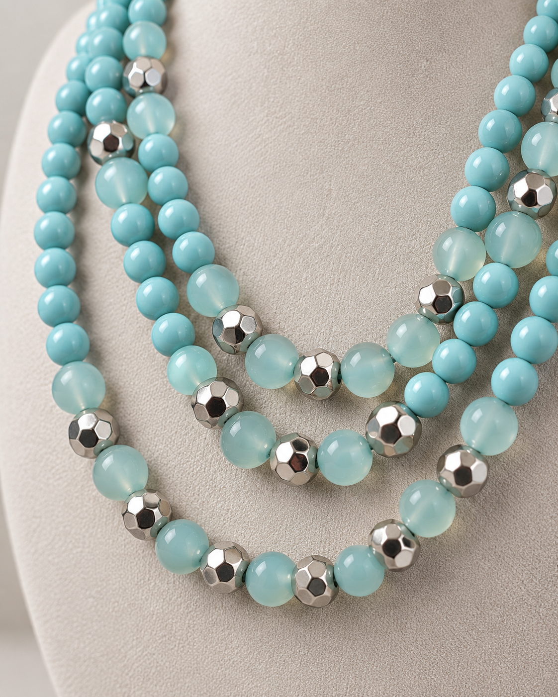 Three-strand aqua and seafoam bead necklace displayed on a neutral linen jewelry bust