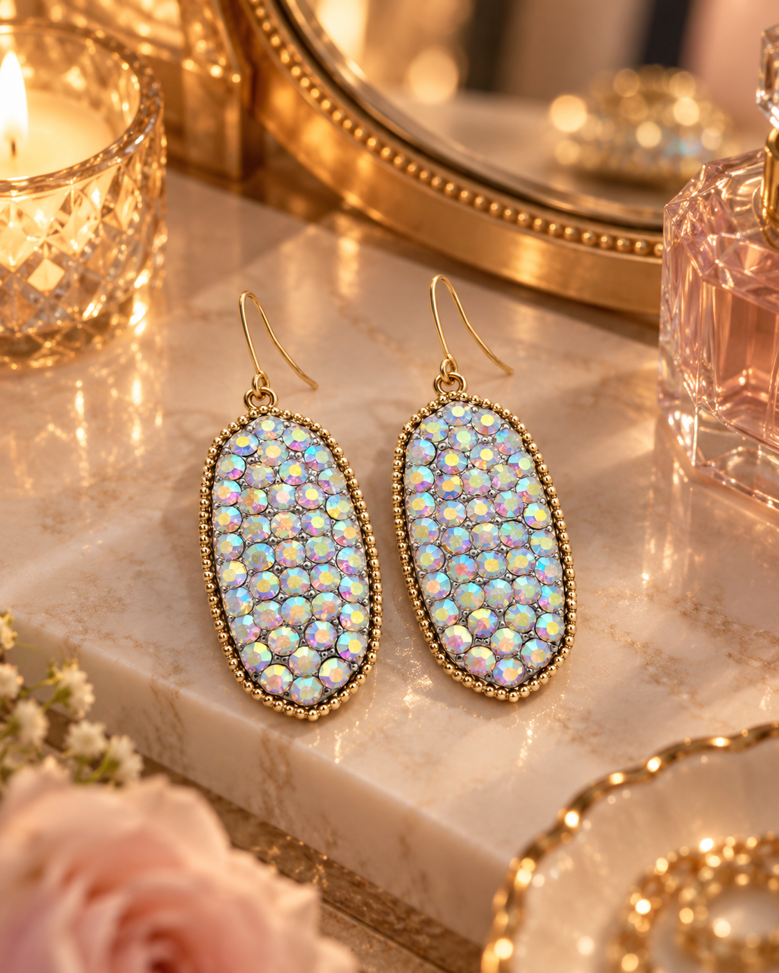 Iridescent gold-tone drop earrings styled on a warm vanity with candlelight and soft blush details