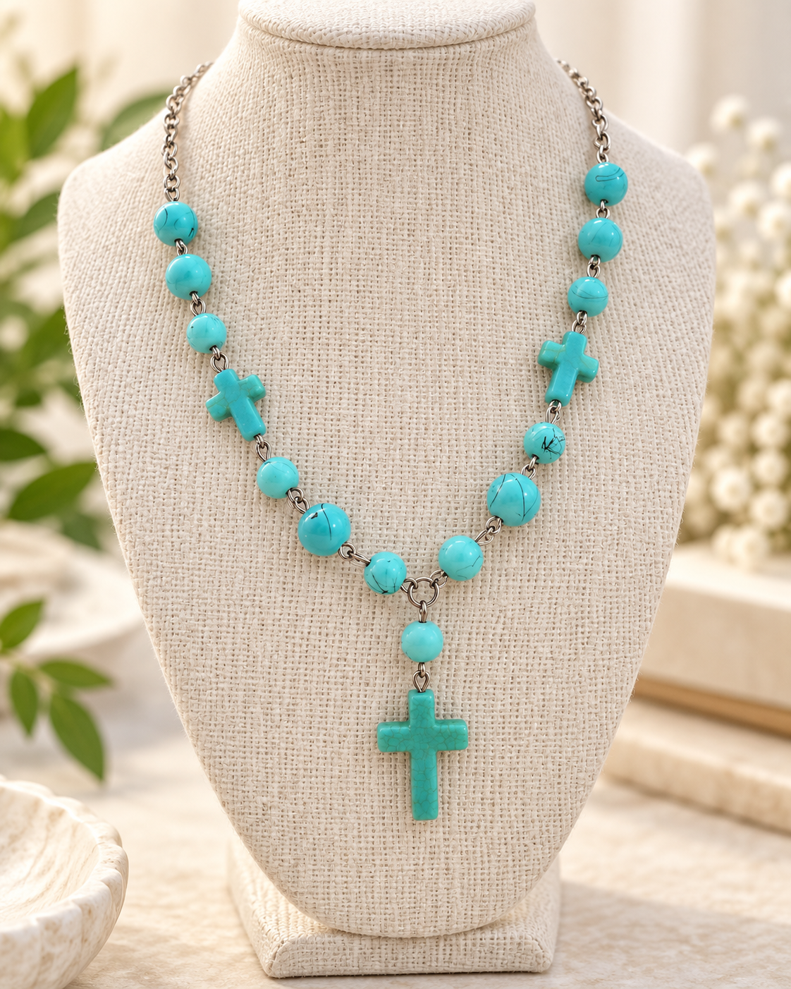 Turquoise-colored bead cross necklace displayed on a neutral linen jewelry bust with silver-tone chain