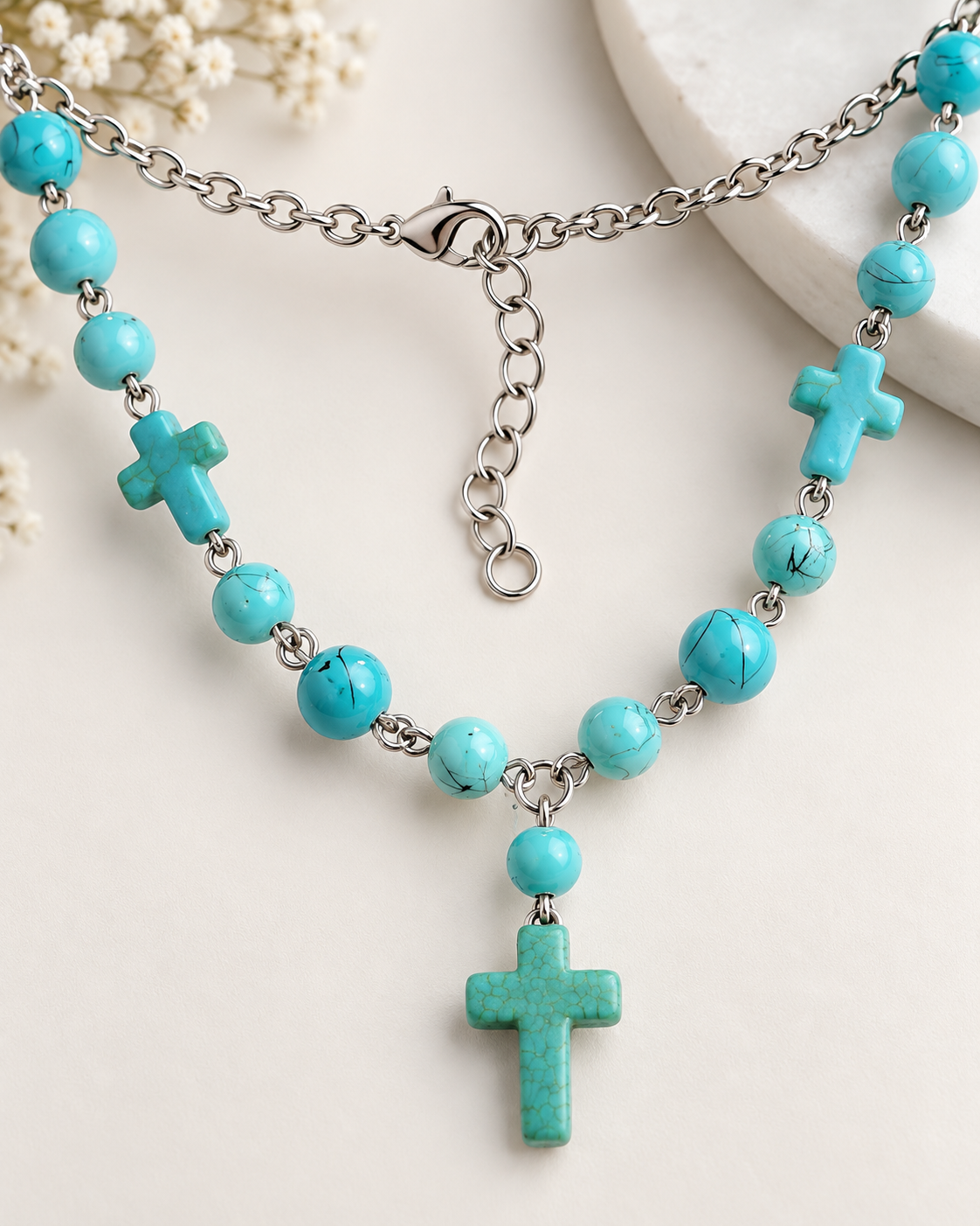 Close-up of silver-tone lobster clasp and extender chain on turquoise-colored cross necklace