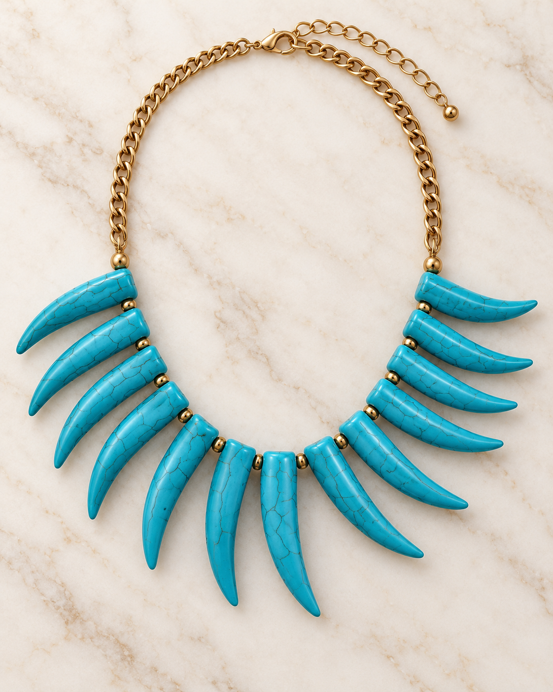 A statement bib necklace featuring twelve curved turquoise-colored tooth-like beads attached to a gold-tone chain, displayed on a light beige marble background.
