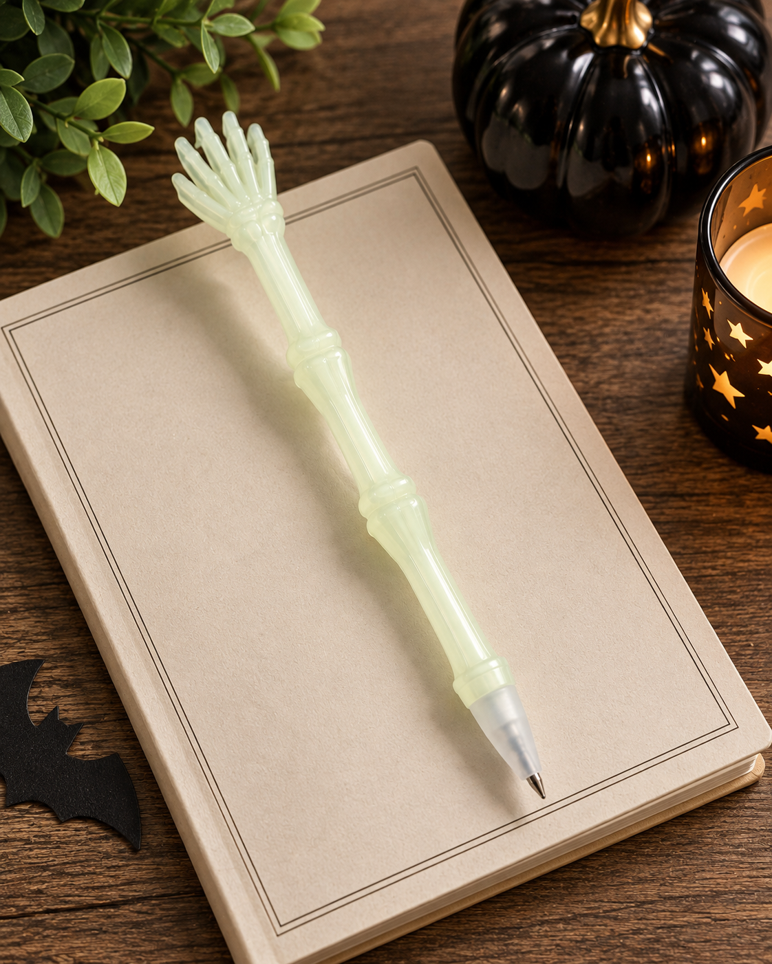 Glow-in-the-dark skeleton hand pen styled on a neutral notebook with black pumpkin and candlelight