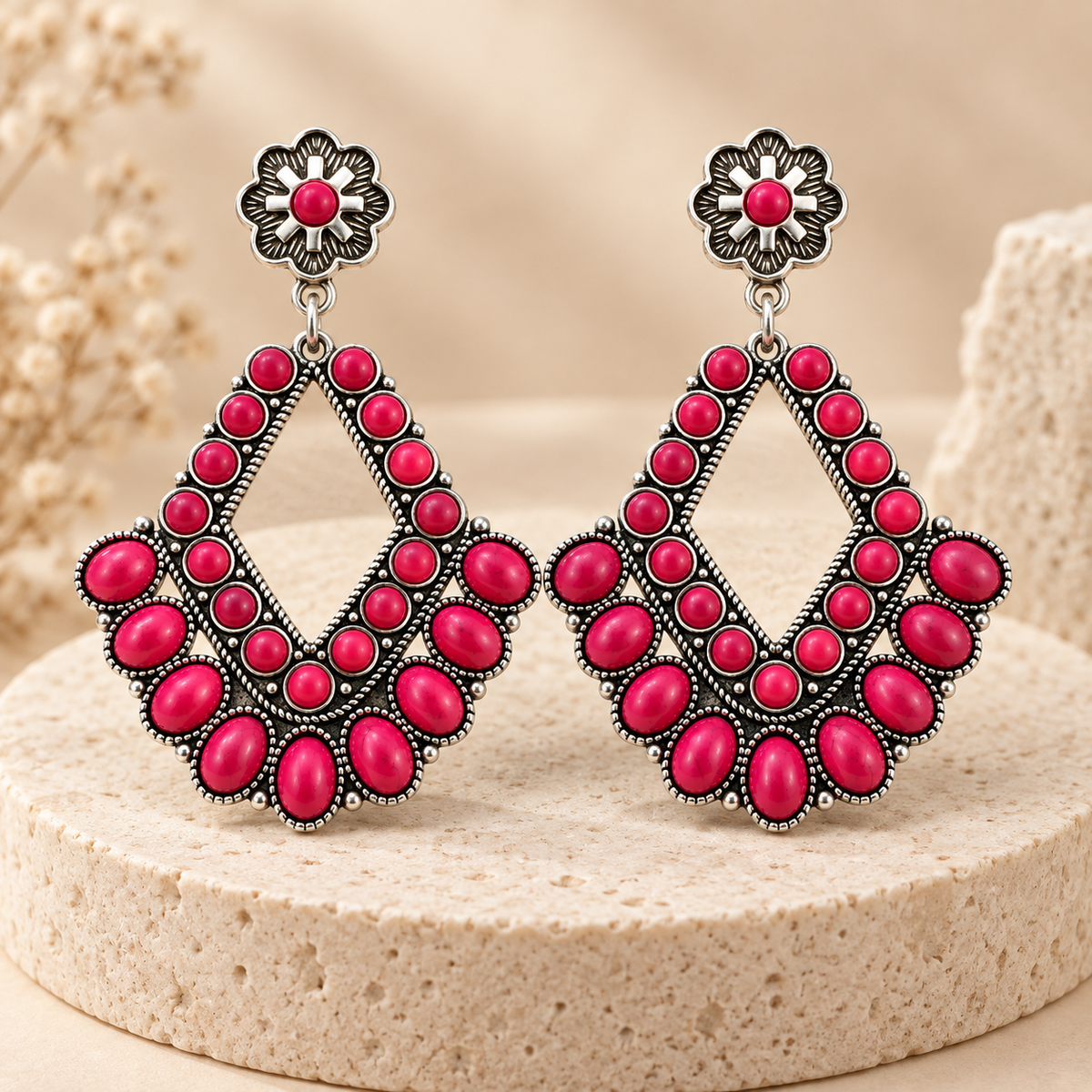 Pink stone diamond-shaped western statement earrings displayed on a neutral stone pedestal