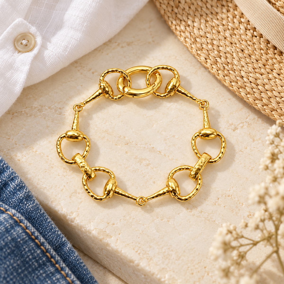 Golden equestrian horse bit link bracelet flat lay styled with white linen, straw hat, and denim