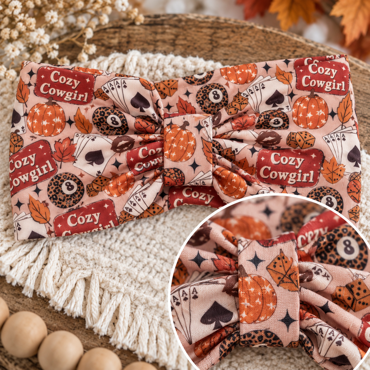 A fabric headband with a large bow, featuring a cozy autumn-themed print with pumpkins, playing cards, leaves, and donuts. The print includes the text 'Cozy Cowgirl' on red labels.