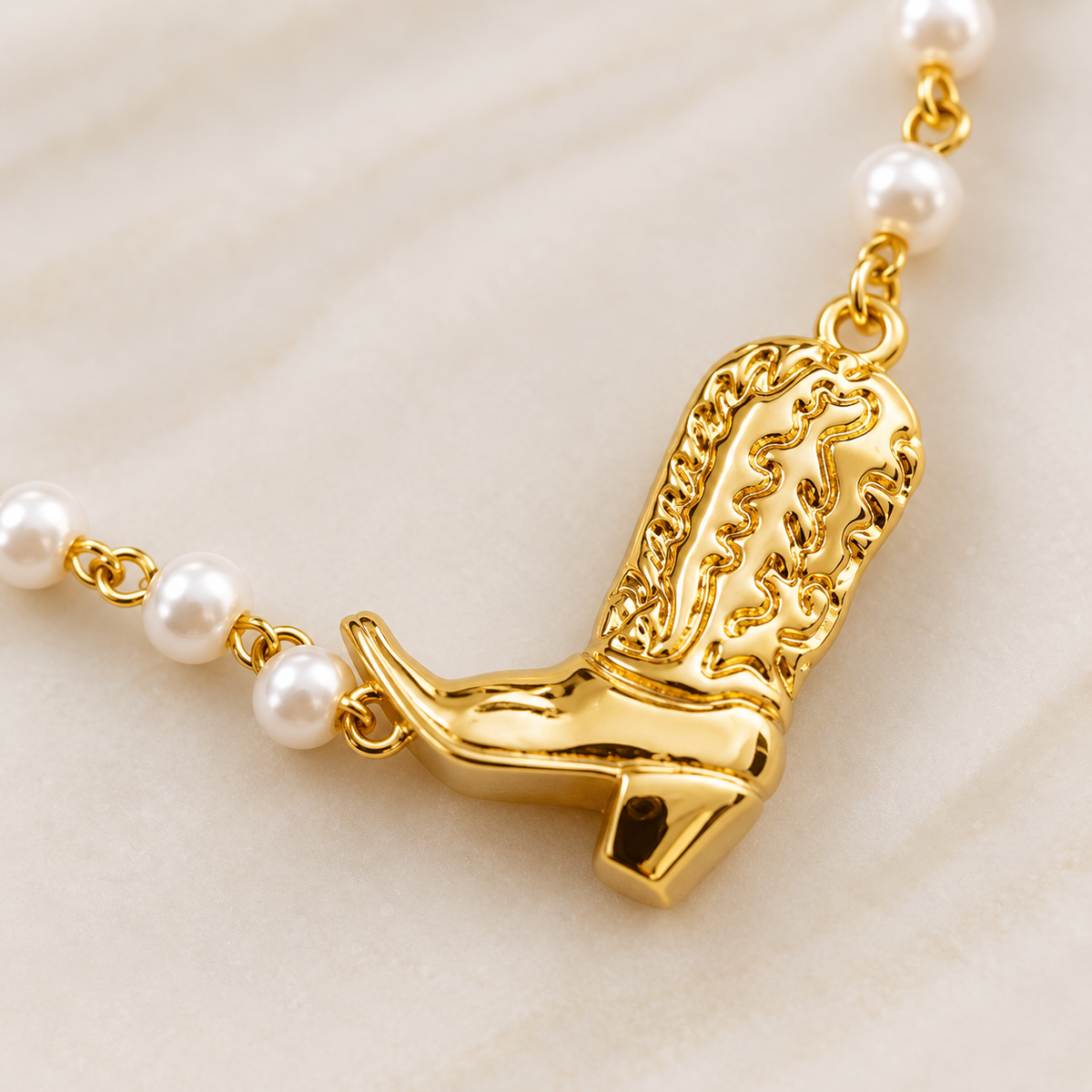 Close-up of gold cowgirl boot pendant with glass pearl chain detail