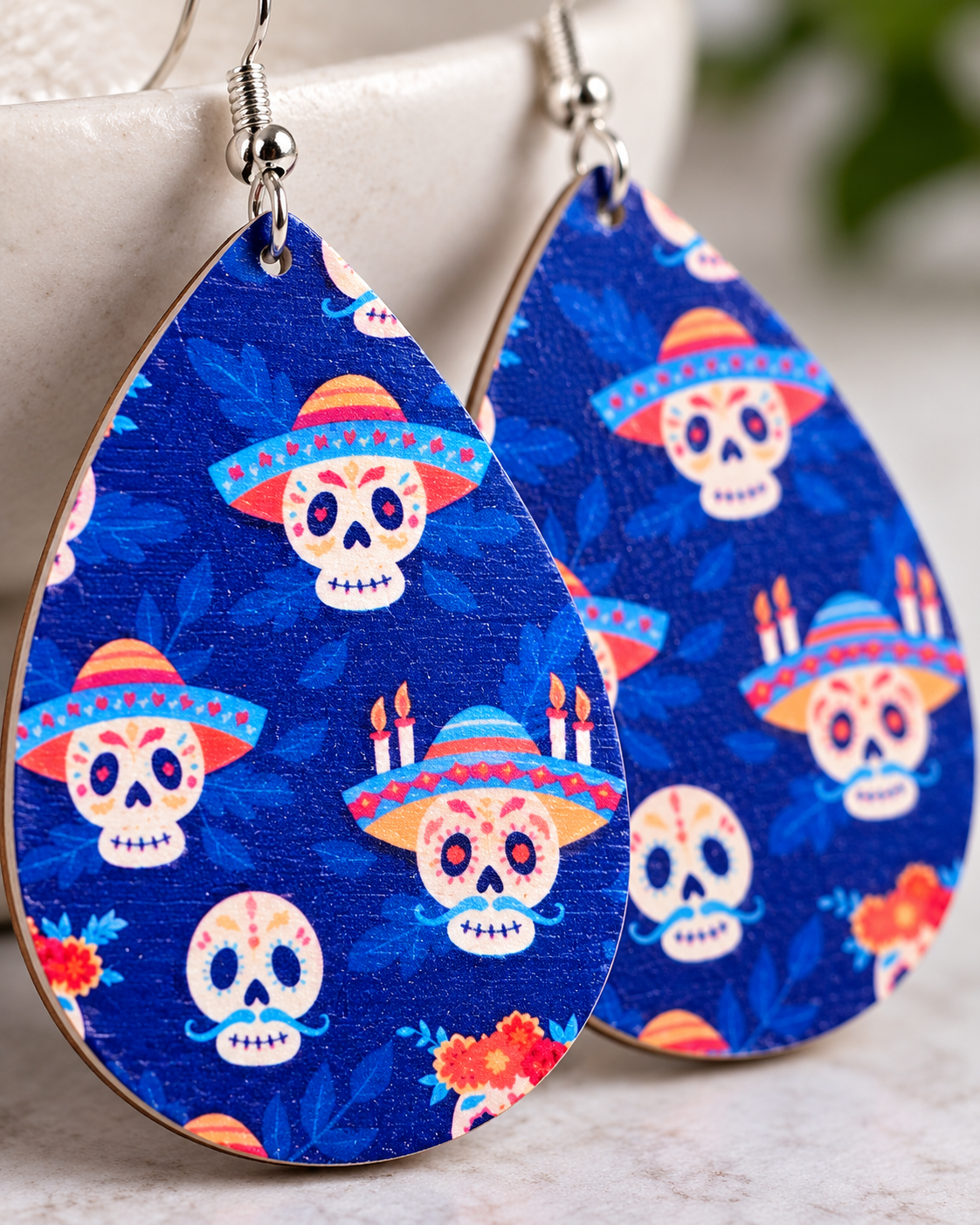Close-up of cobalt-blue wood earrings showing colorful skull, sombrero, floral, and candle details