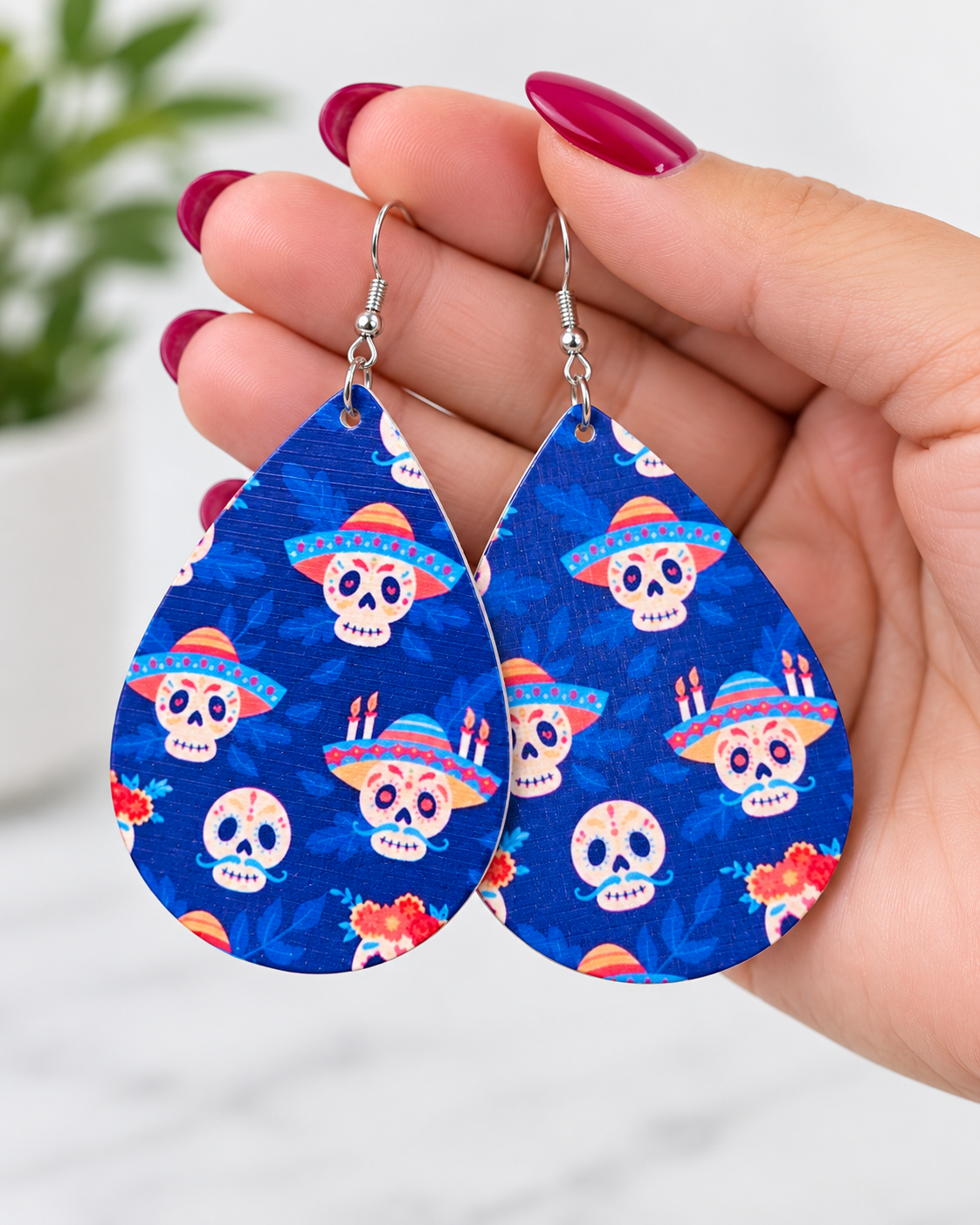 Blue sugar skull wood teardrop earrings held in hand to show scale, color, and lightweight statement size