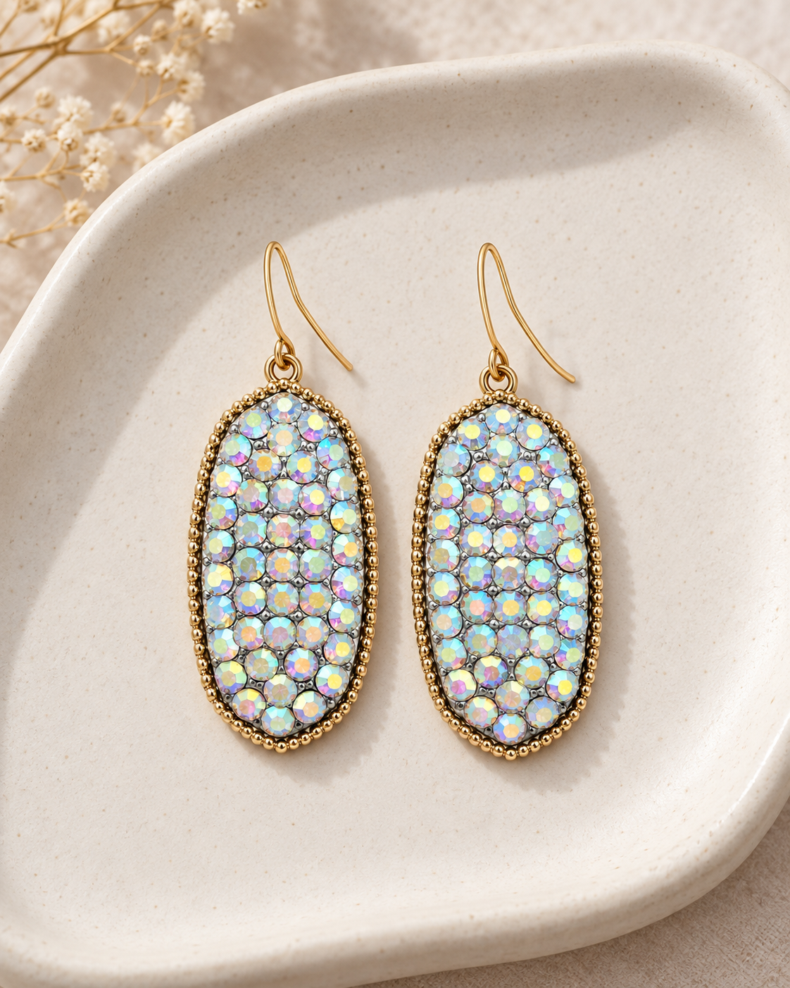 Iridescent drop earrings styled on a neutral ceramic tray with soft cream accents