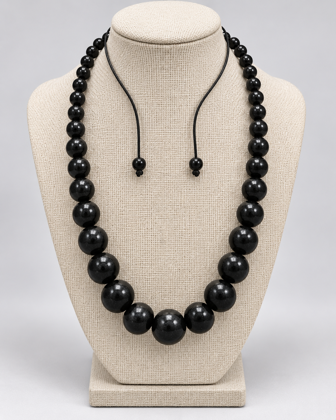 Graduated black bead statement necklace displayed on a neutral linen jewelry bust