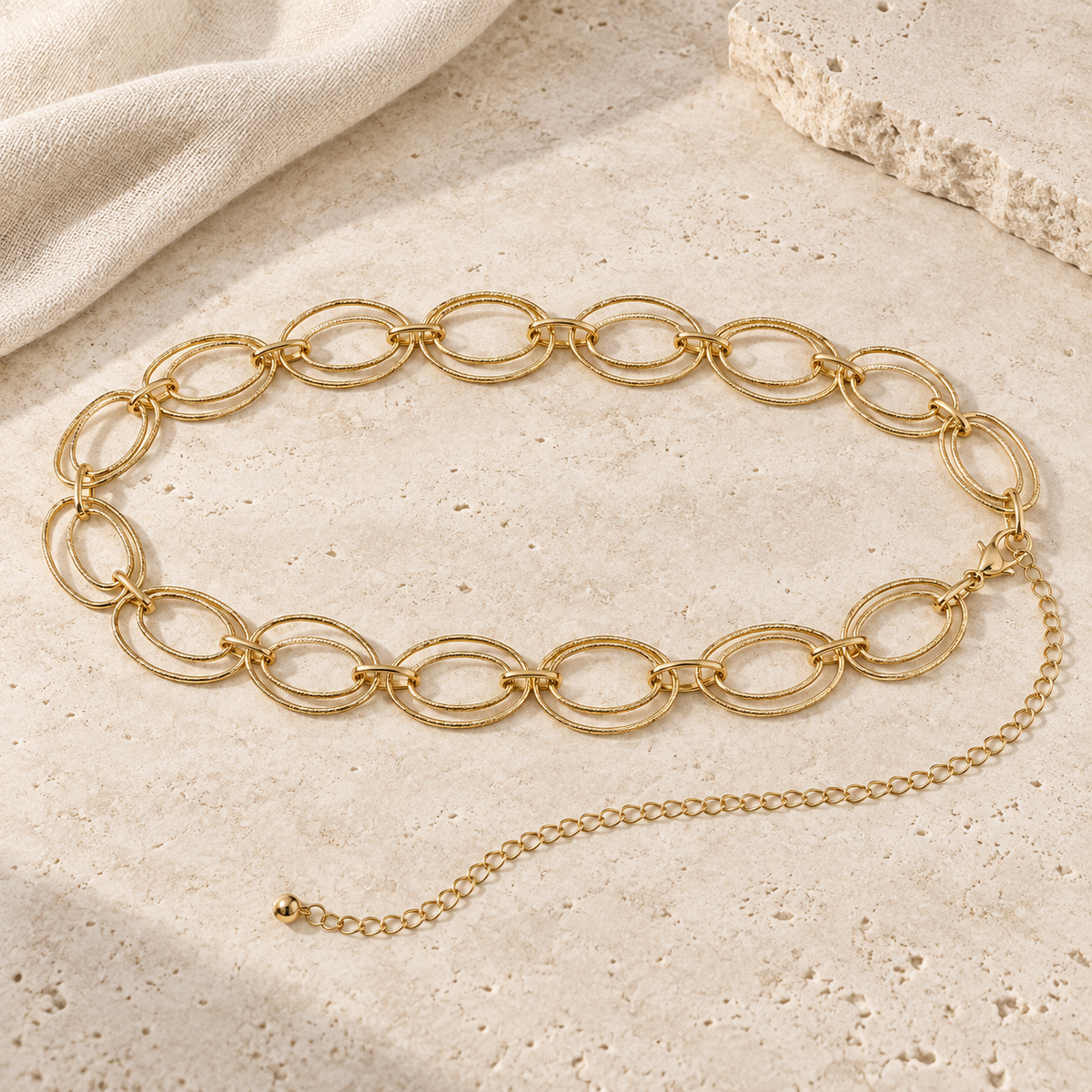 Gold-tone Uptown Links layered oval waist chain belt displayed on ivory stone with soft linen.