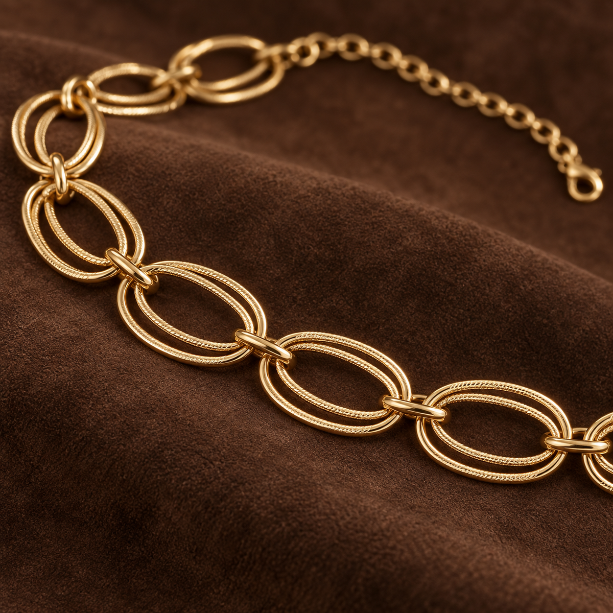 Close-up of the gold-tone double oval links displayed on rich brown suede.