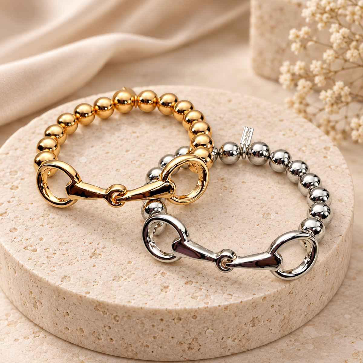 Gold-tone and silver-tone snaffle bit bracelets displayed on a neutral stone pedestal