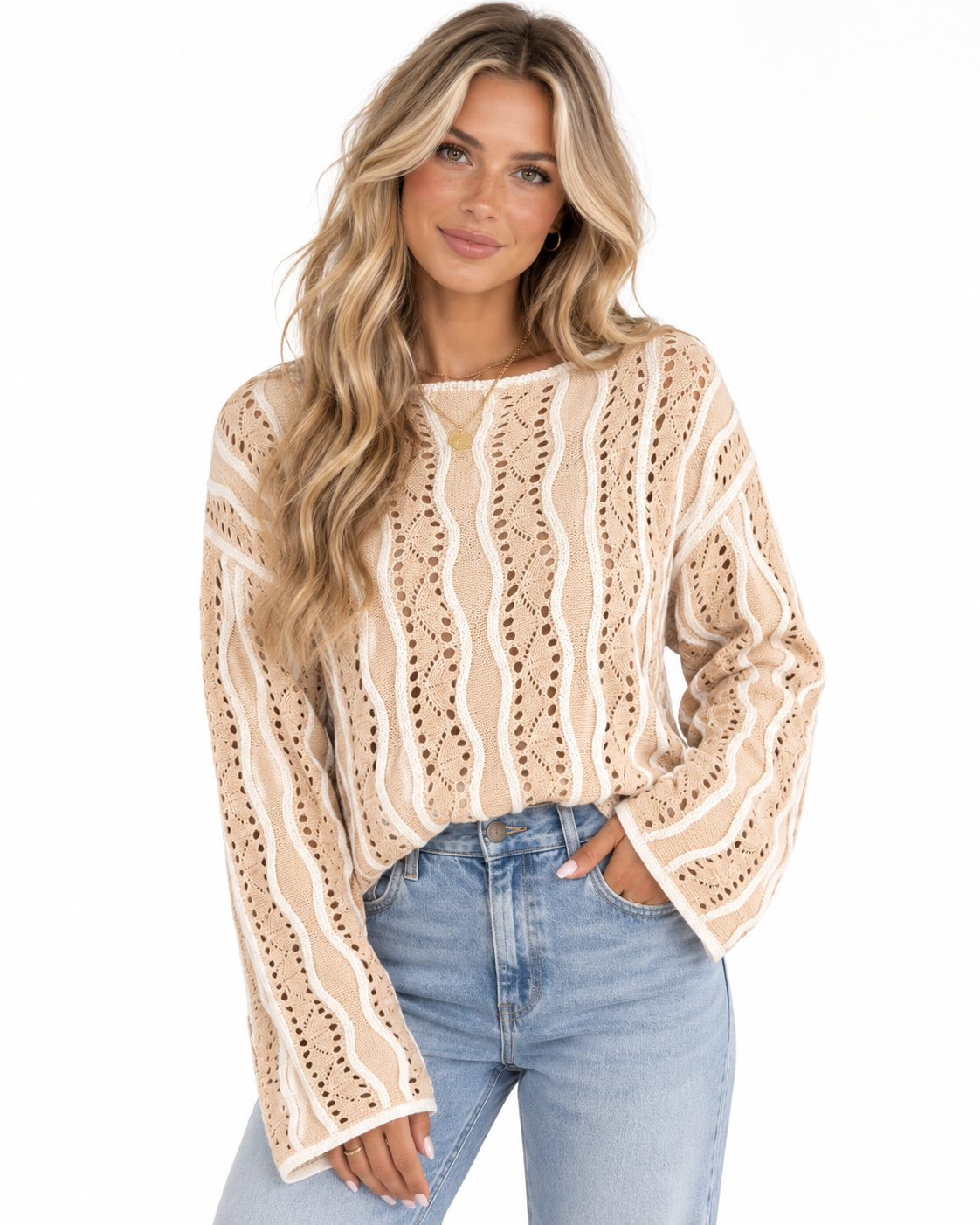 A woman modeling a beige and white patterned knit sweater with bell sleeves, paired with light blue jeans, against a plain white background.