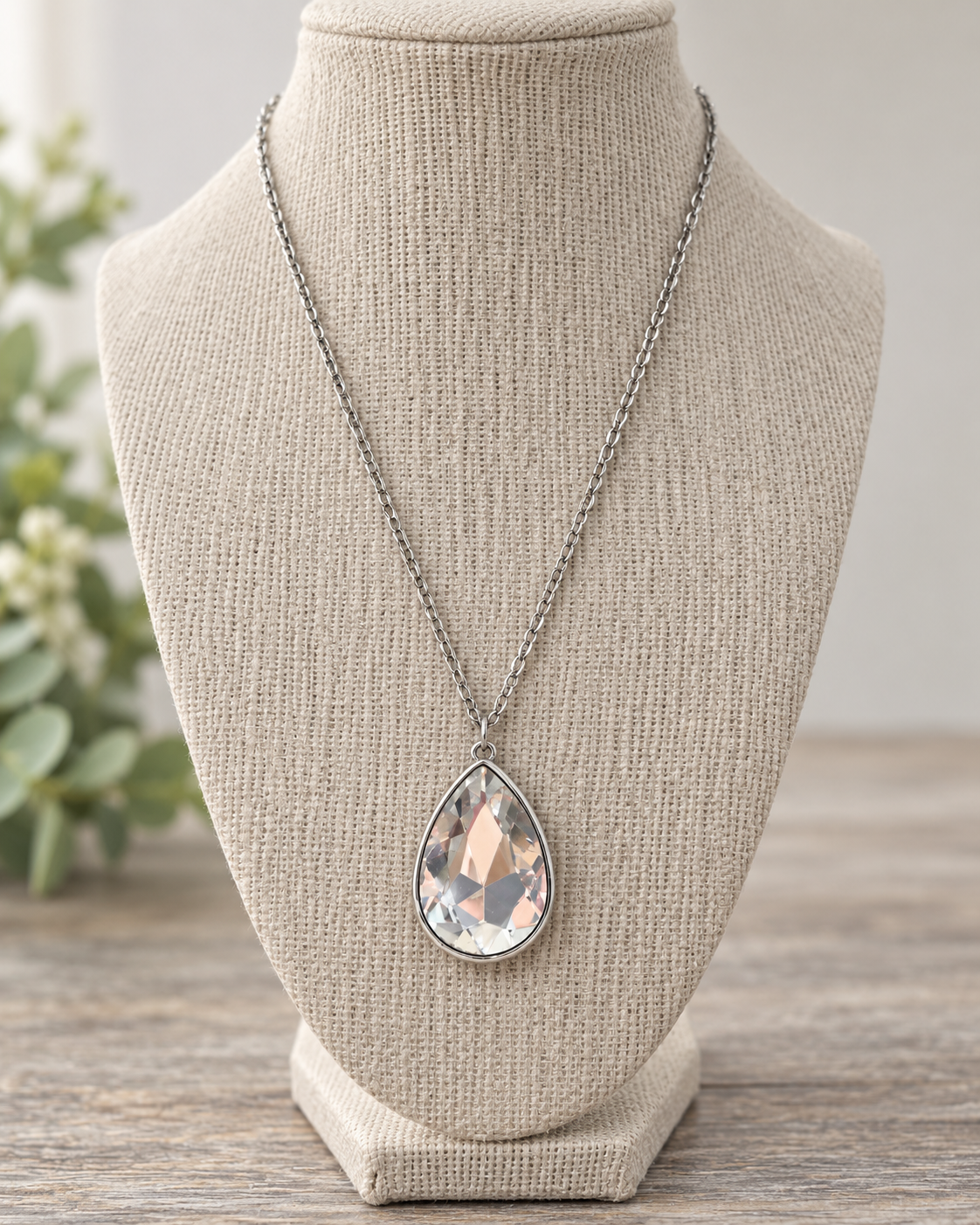 Clear faceted teardrop pendant necklace displayed on a neutral linen jewelry bust
