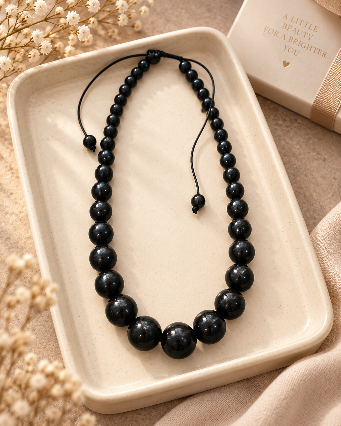 Graduated black bead necklace styled in a cream ceramic tray with soft neutral gift-ready details