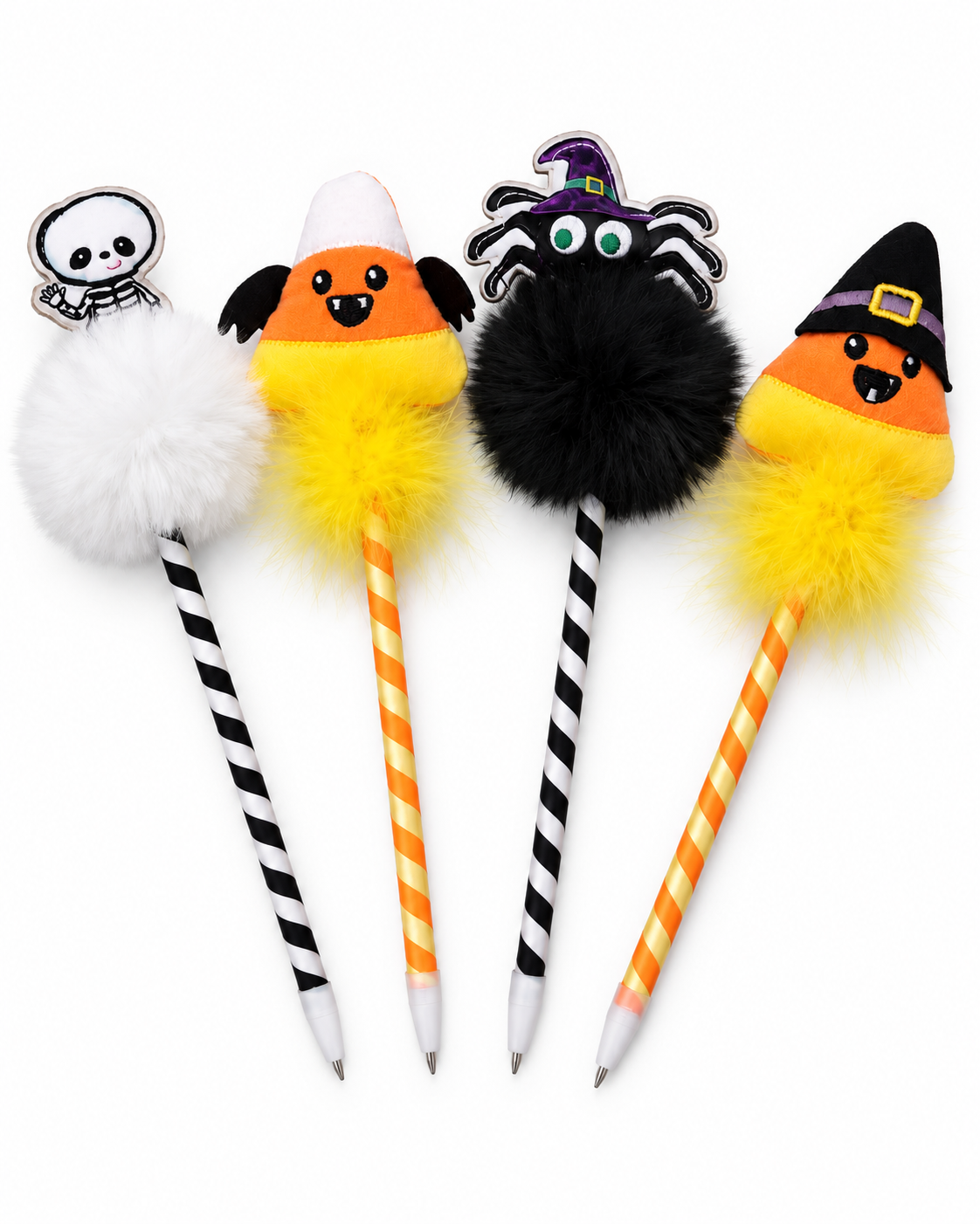 Four Halloween-themed novelty pens with plush decorative tops: a white skull on a black-and-white striped pen, a candy corn with a white pom-pom on an orange-and-white striped pen, a black spider with a purple witch hat on a black-and-white striped pen, and a candy corn with a yellow pom-pom on an orange-and-yellow striped pen.