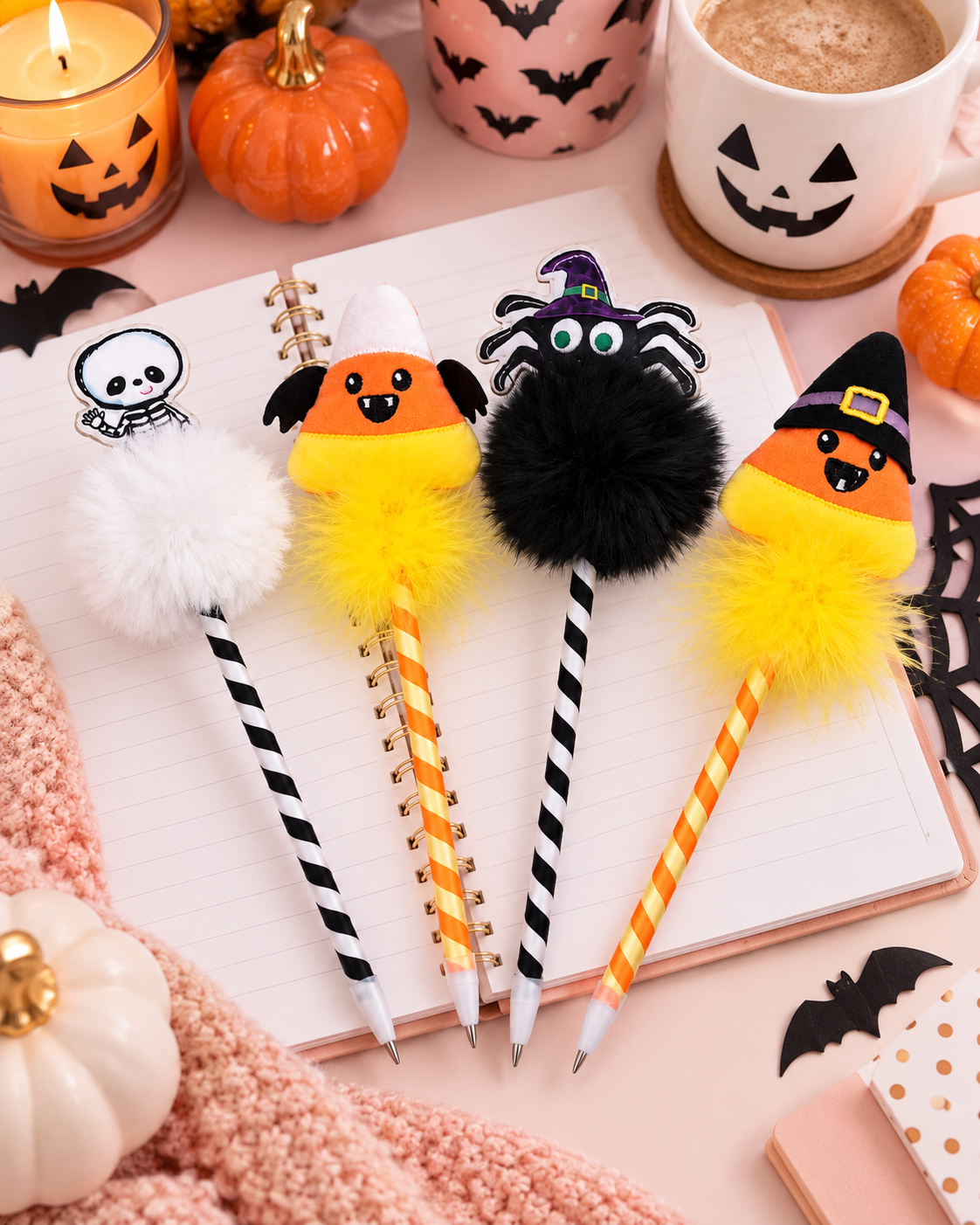 Four Halloween-themed decorative pencils arranged on an open notebook in a styled flat lay. The pencils feature fluffy pom-poms, candy corn, a black spider, and a witch hat design, with striped handles and white tips.
