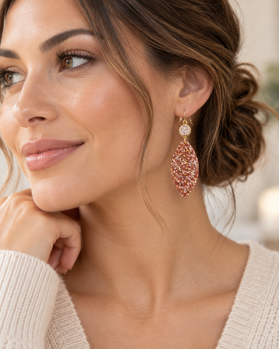 Lifestyle image of woman wearing Rosé Glow glitter leaf earrings with a soft ivory sweater and swept-back hair