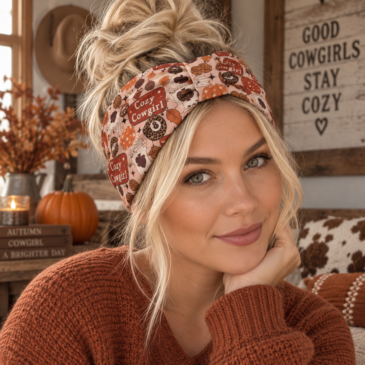 A woman wearing a cozy autumn-themed fabric headband with a cowgirl print, paired with a rust-colored knit sweater in a warm, rustic room setting.