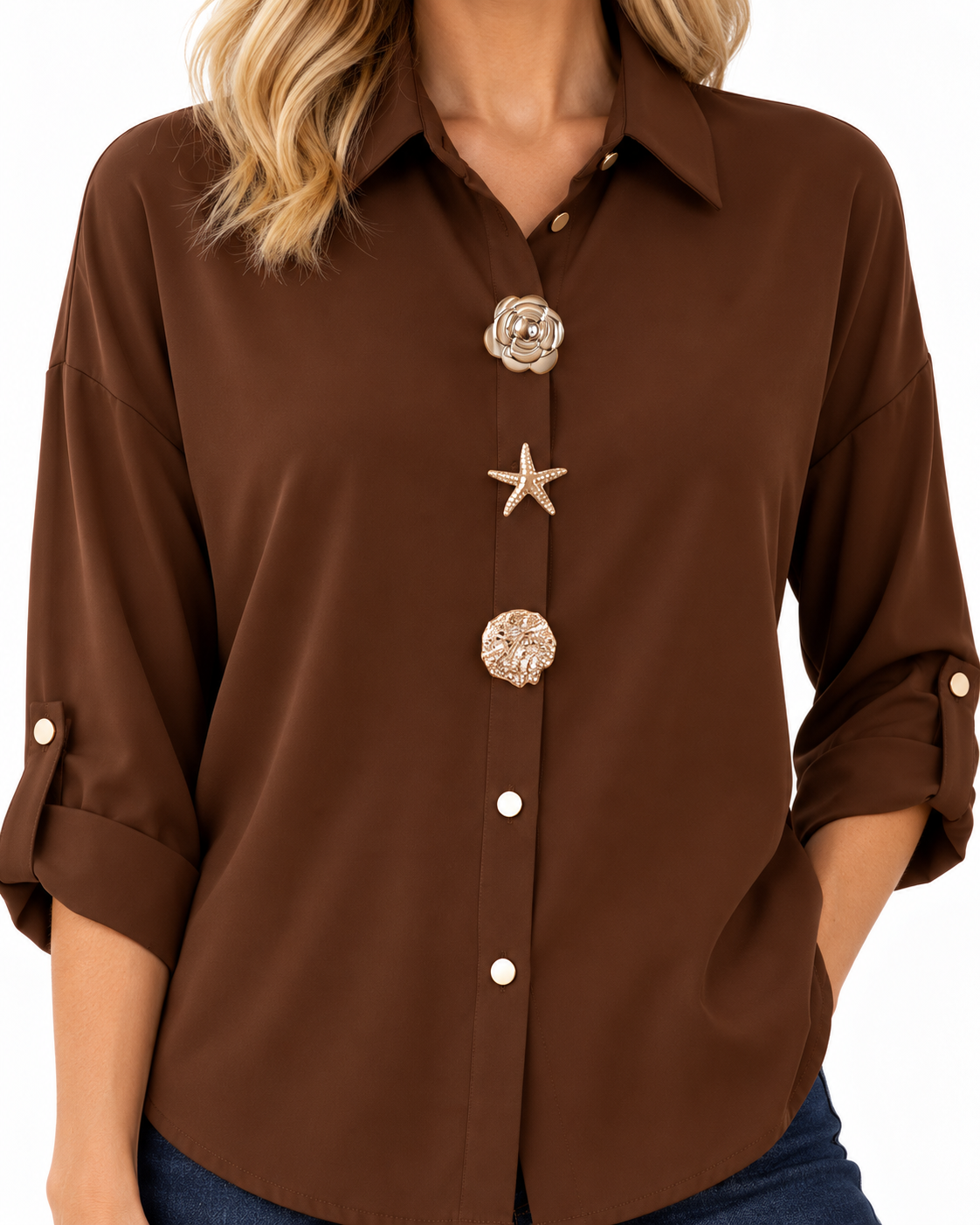 A woman wearing a brown button-down shirt with decorative shell-style buttons, shown from the shoulders to the hips against a plain white background.