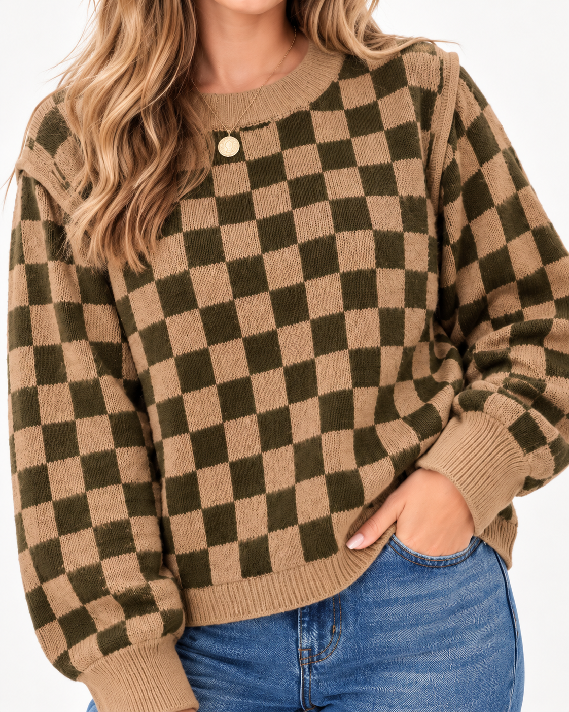 A woman wearing a brown and olive green checkerboard knit sweater with a single gold button at the collar, paired with blue jeans.