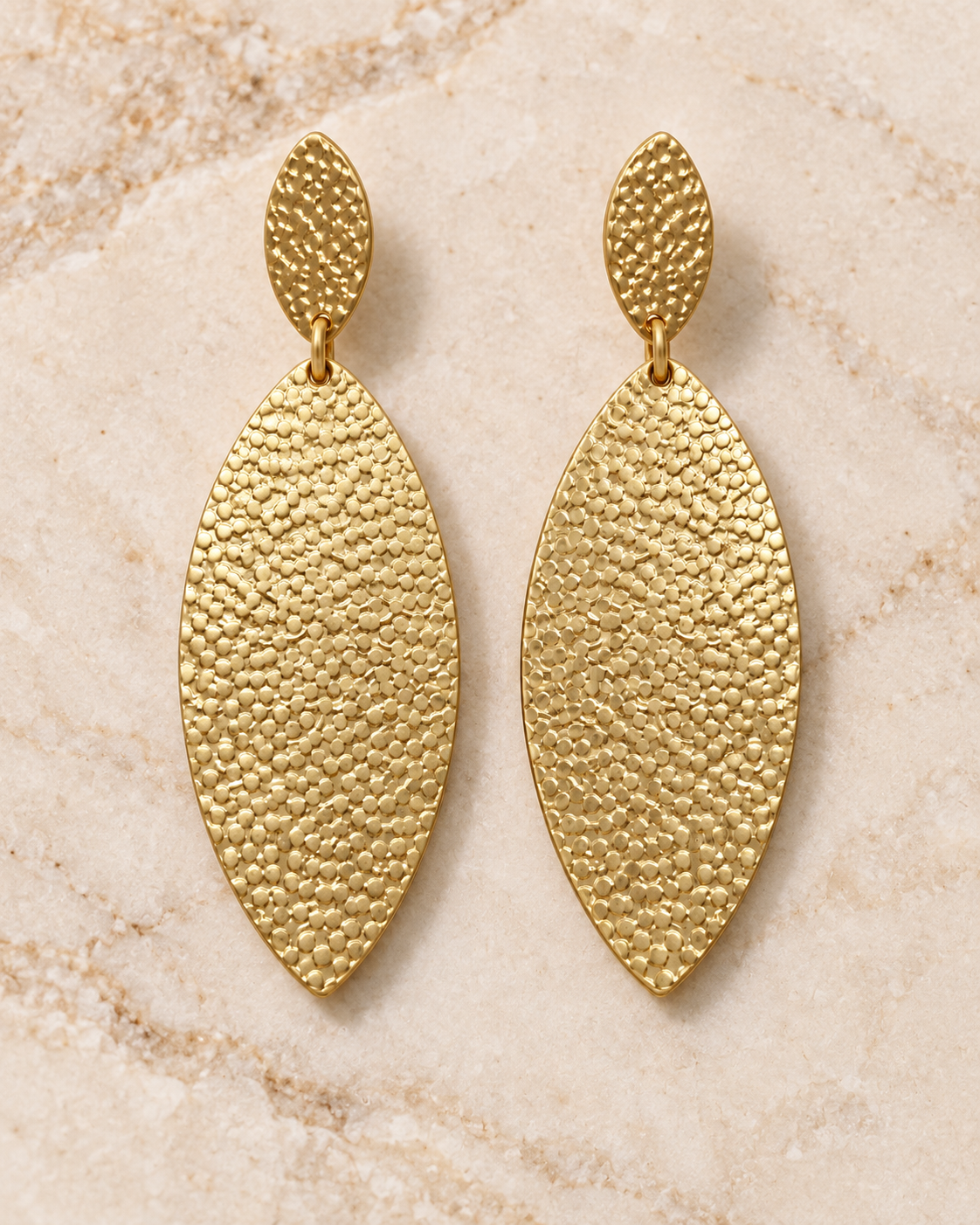 Textured gold-tone statement earrings styled on a soft cream marble surface
