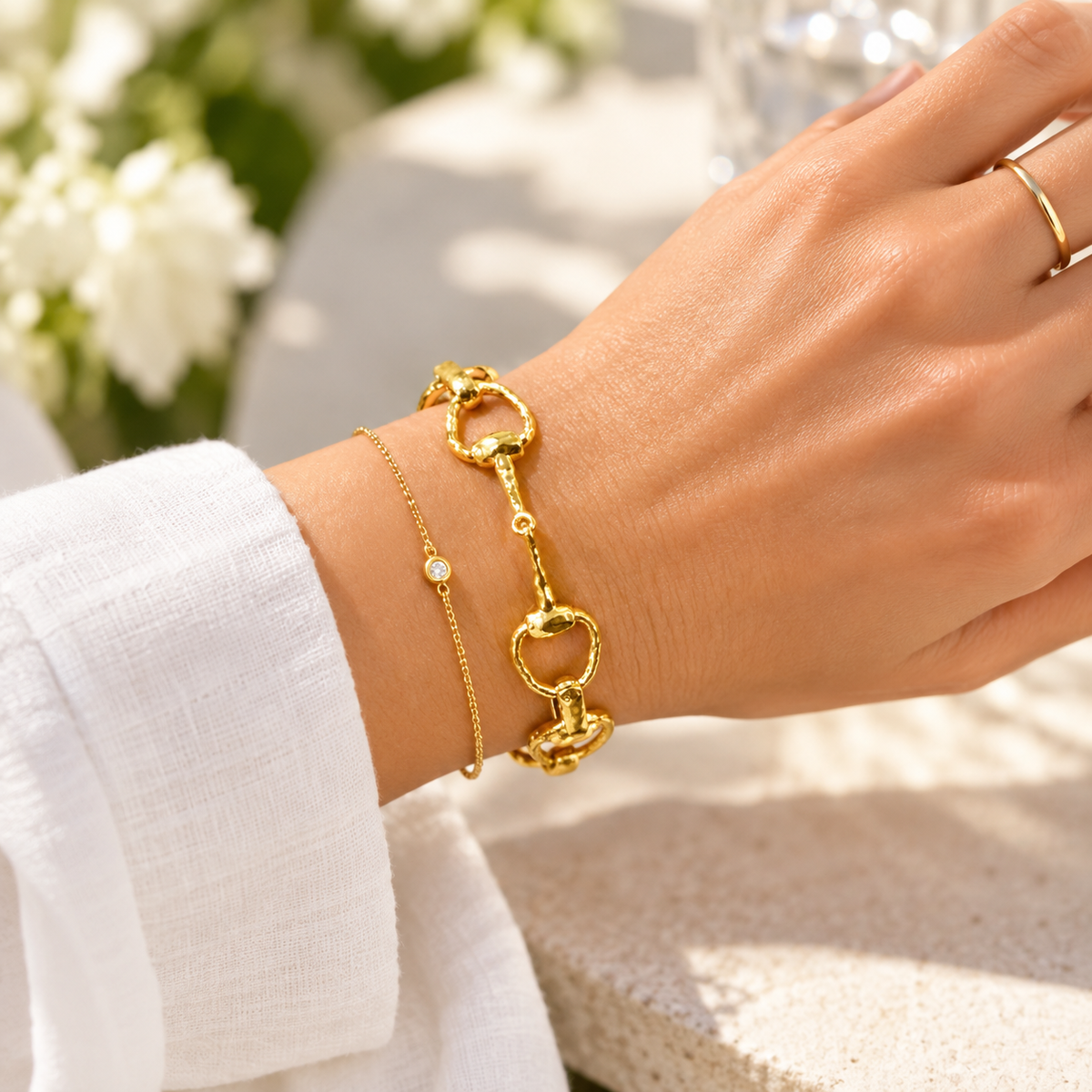 Close-up of golden equestrian horse bit link bracelet layered with a delicate gold chain bracelet