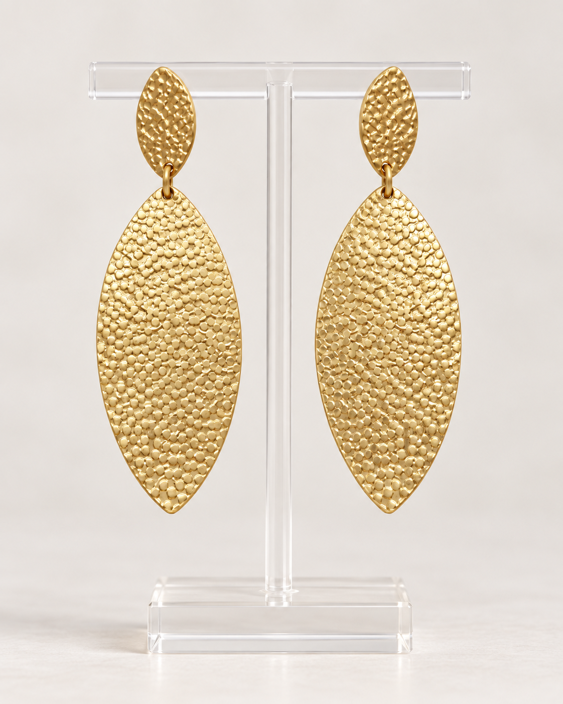 Textured gold-tone drop earrings displayed on a clear jewelry stand with elongated oval silhouette
