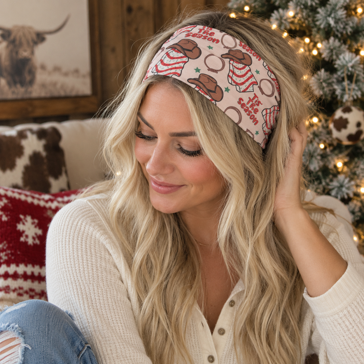 A woman wearing a festive holiday-themed fabric headband with a brown bear and snowman pattern, sitting in a cozy living room setting with a Christmas tree in the background.