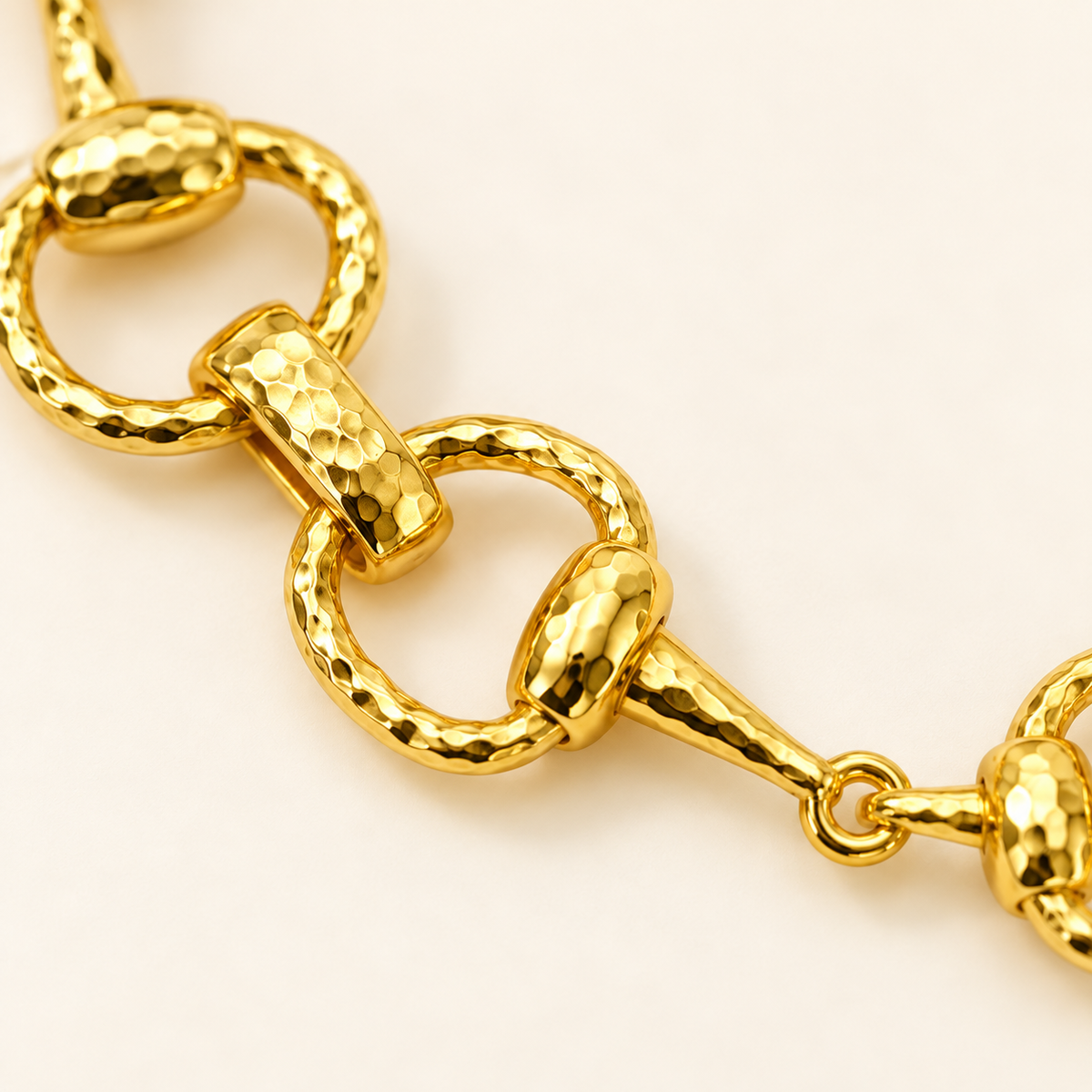 Close-up of golden equestrian horse bit link bracelet showing hammered texture and polished link detail