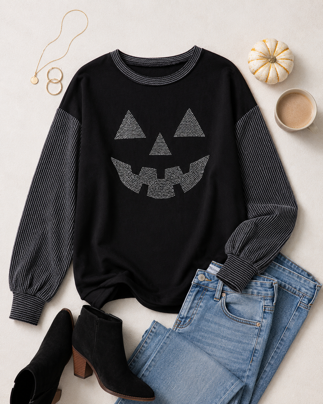 Flat lay of the black rhinestone pumpkin top with blue denim, black ankle boots, gold jewelry, coffee, and a mini white pumpkin.