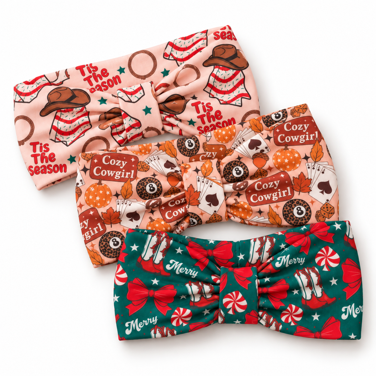 Three knotted fabric headbands with holiday and western cowgirl prints, arranged diagonally on a white background. The top headband is light pink with 'Tis The Season' cowgirl motifs.
