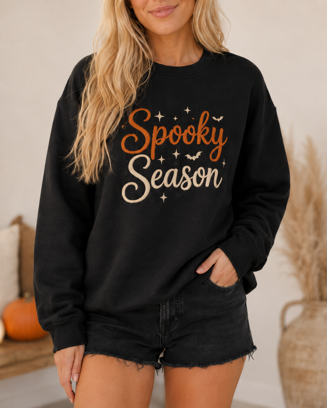 Close-up of the black Spooky Season sweatshirt showing the orange and cream embroidered lettering and seasonal details.