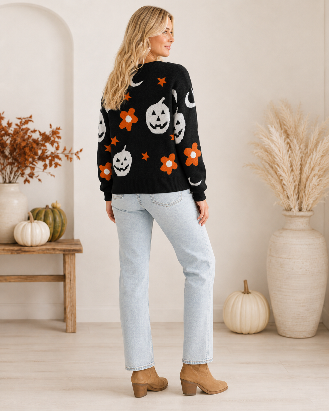 Back view of Emma wearing the black Halloween sweater featuring white jack-o'-lanterns, crescent moons, orange stars and flowers.