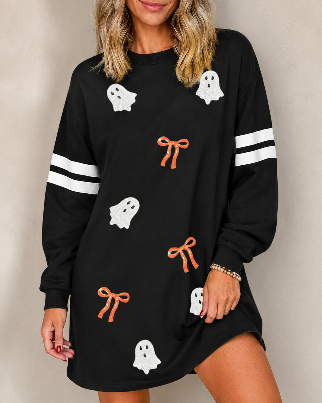 Close-up of the Ghost & Bow Varsity Sweatshirt Dress showing white ghost details, orange bows, crew neckline, and varsity sleeve stripes.
