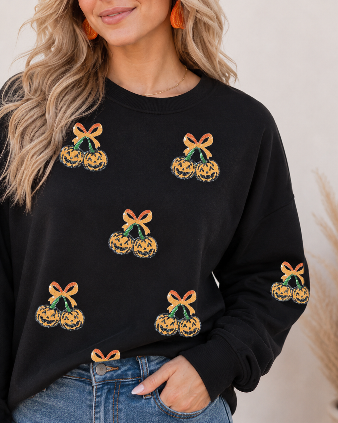 Close-up of the black Halloween sweatshirt showing sequin pumpkin pairs, orange bow details, crew neckline, and ribbed cuffs.