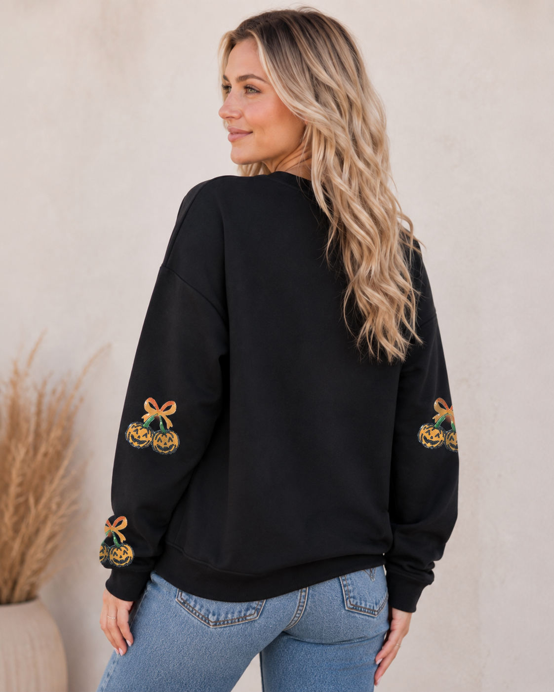 Back view of the black Pumpkin Bow Sequin Sweatshirt showing the relaxed silhouette, ribbed hem, and pumpkin graphics along the sleeves.