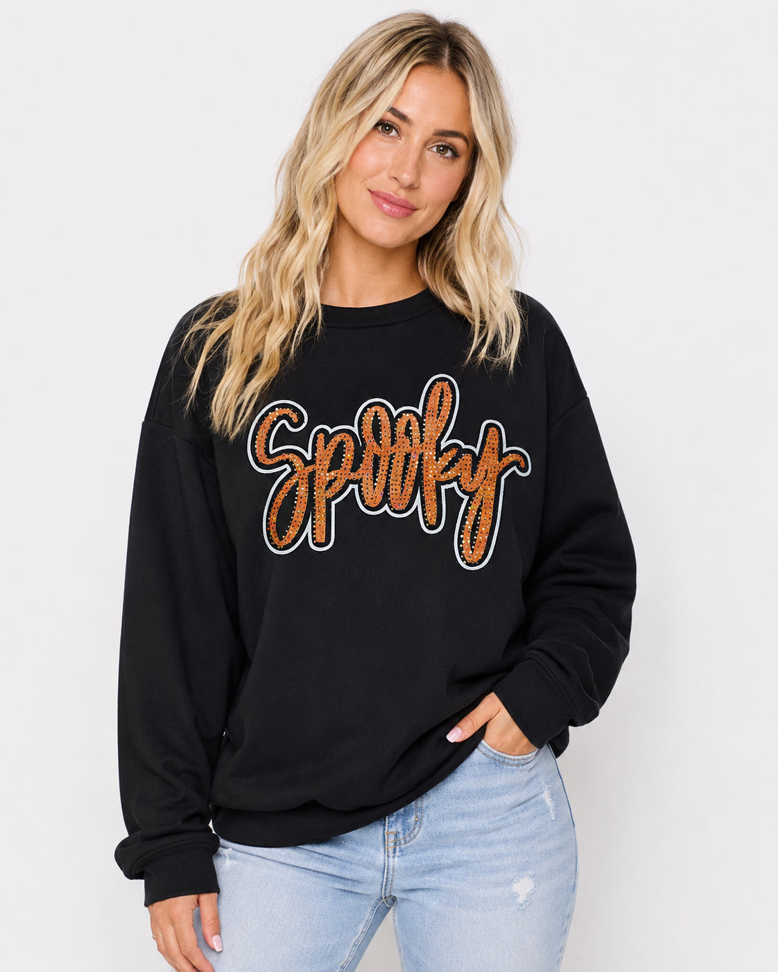 Black Spooky Rhinestone Sweatshirt with orange rhinestone script graphic styled with light-wash denim on a clean white background.