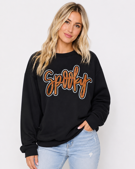 Black Spooky Rhinestone Sweatshirt with orange rhinestone script graphic styled with light-wash denim on a clean white background.