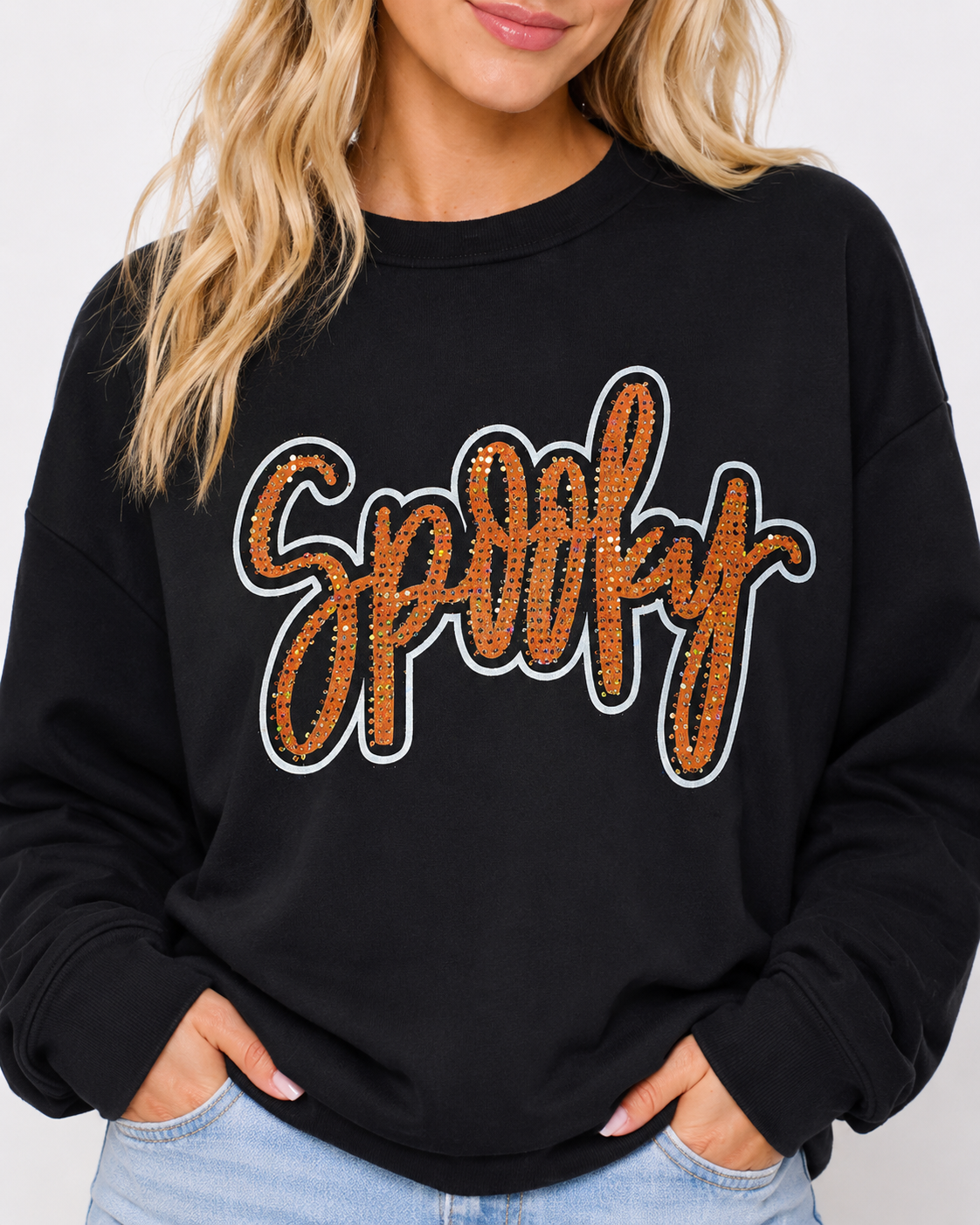 Close-up of the black Spooky Rhinestone Sweatshirt showing the orange rhinestone lettering, crew neckline, and relaxed drop-shoulder fit.
