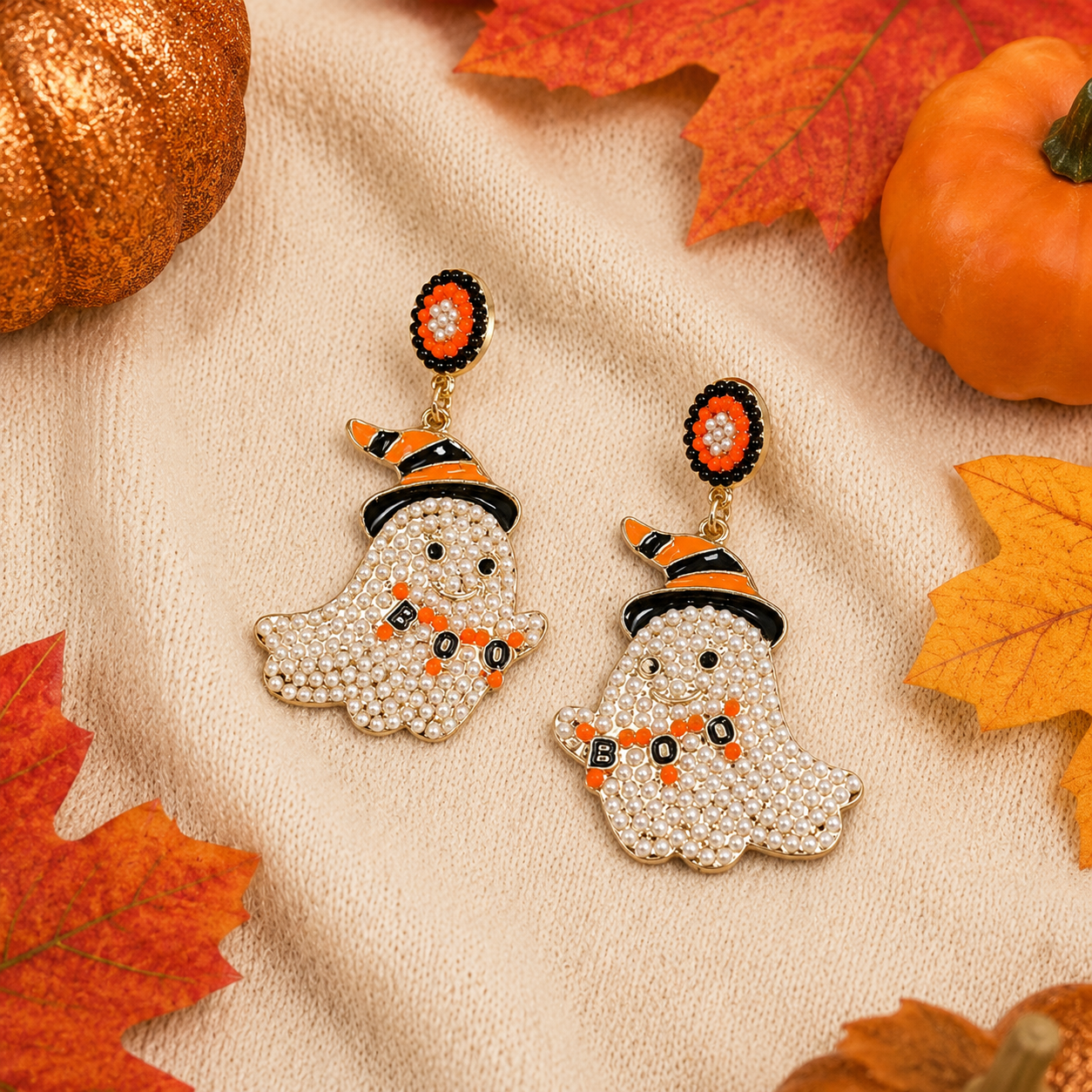 Pearl-covered ghost earrings with orange and black witch hats styled on soft cream fabric