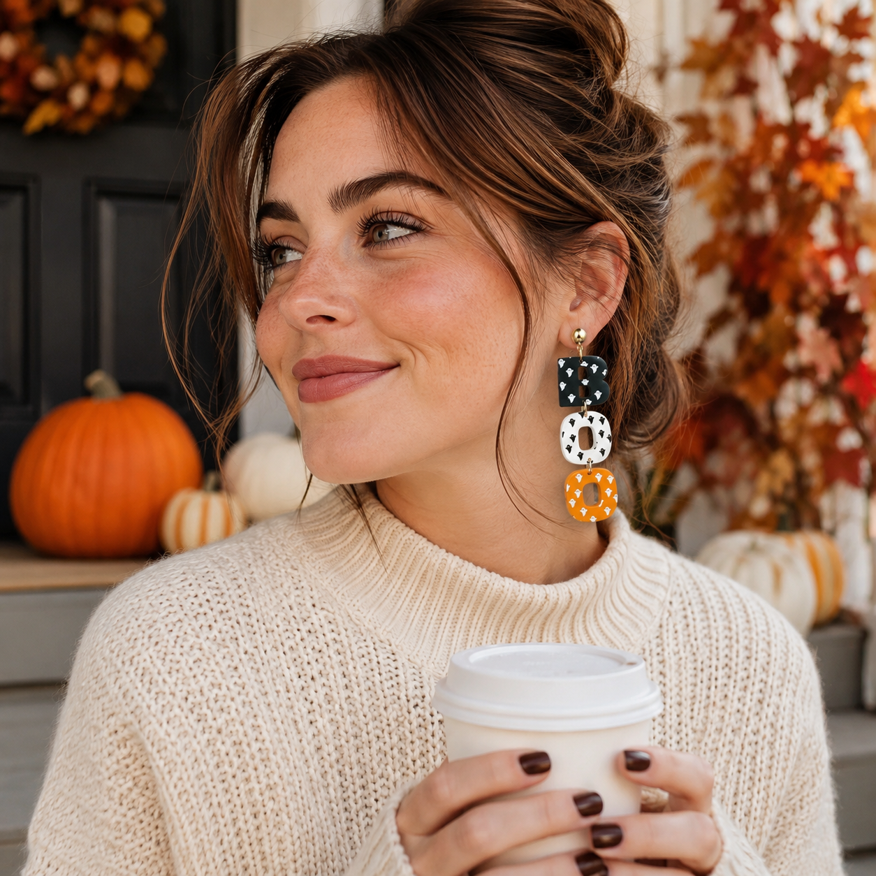 Woman wearing black white and orange BOO earrings while holding coffee in a fall setting