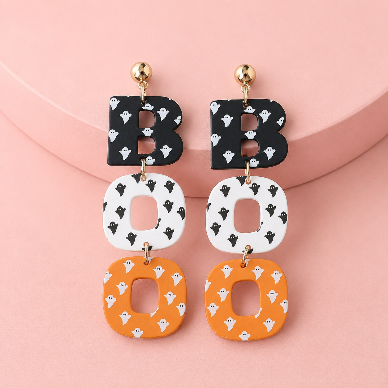 Black white and orange BOO Halloween earrings styled on soft pink background