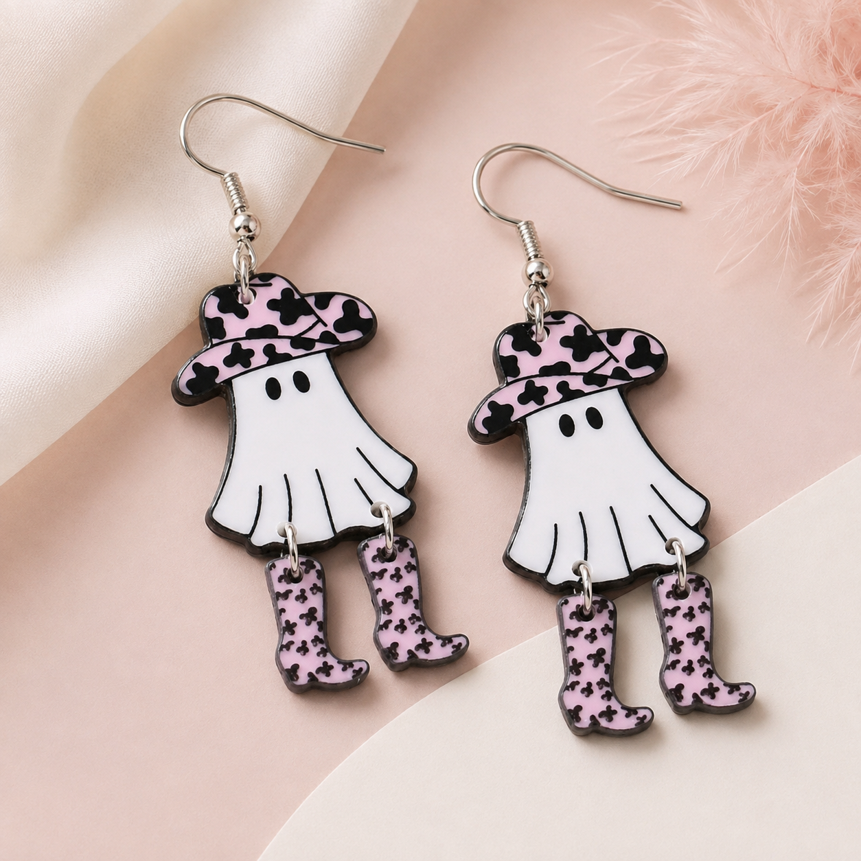 Pink and black cow-print ghost cowboy earrings styled on soft blush background
