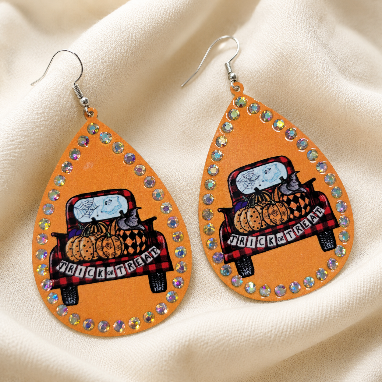 Orange rhinestone Halloween teardrop earrings with pumpkin-filled pickup truck styled on cream fabric