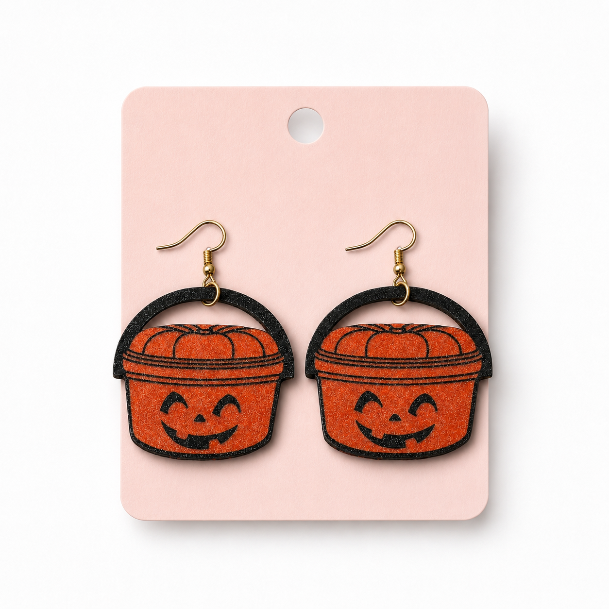 Orange pumpkin pail Halloween dangle earrings displayed on a blush jewelry card against a white background.